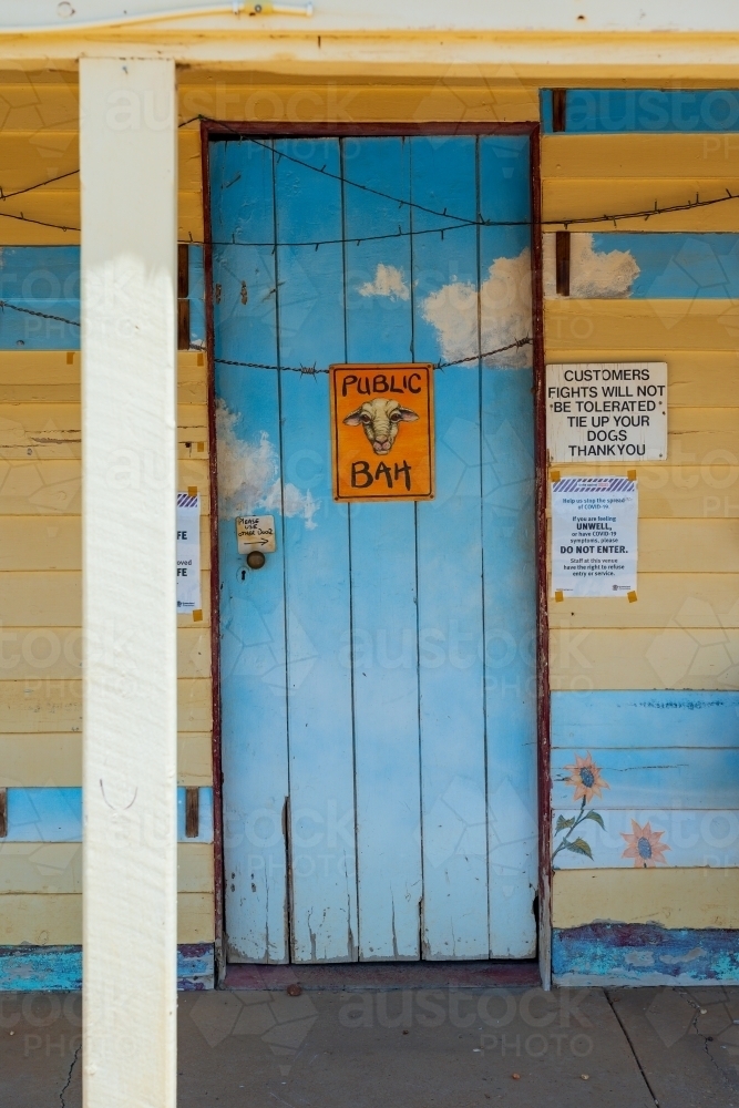 A brightly coloured wooden door with a comical sign on an outback pub - Australian Stock Image