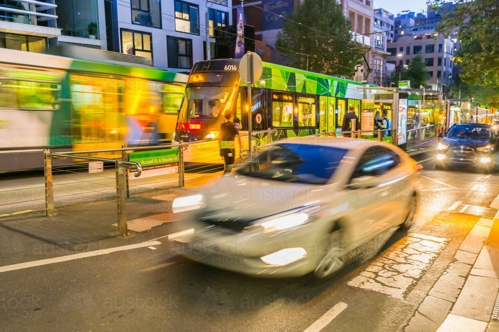 A car speeding past a tram in a city street at night. - Australian Stock Image