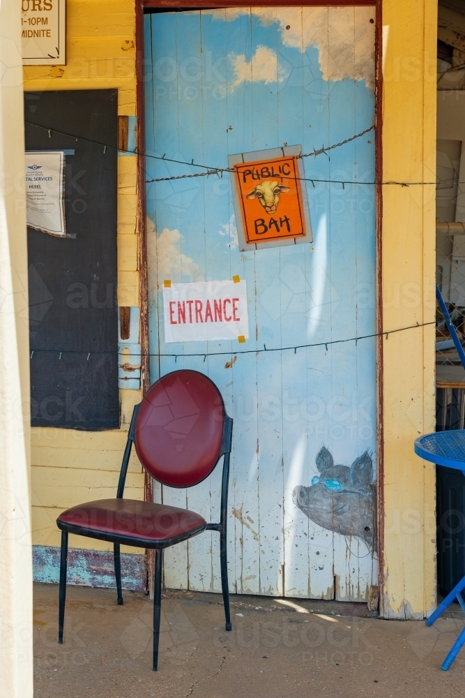 A chair outside a brightly coloured wooden door with a comical sign on an outback pub - Australian Stock Image