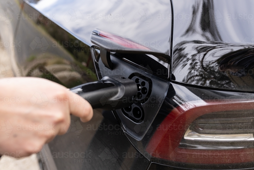 A close up of a EV charger plug being plugged into an electric vehicle car - Australian Stock Image