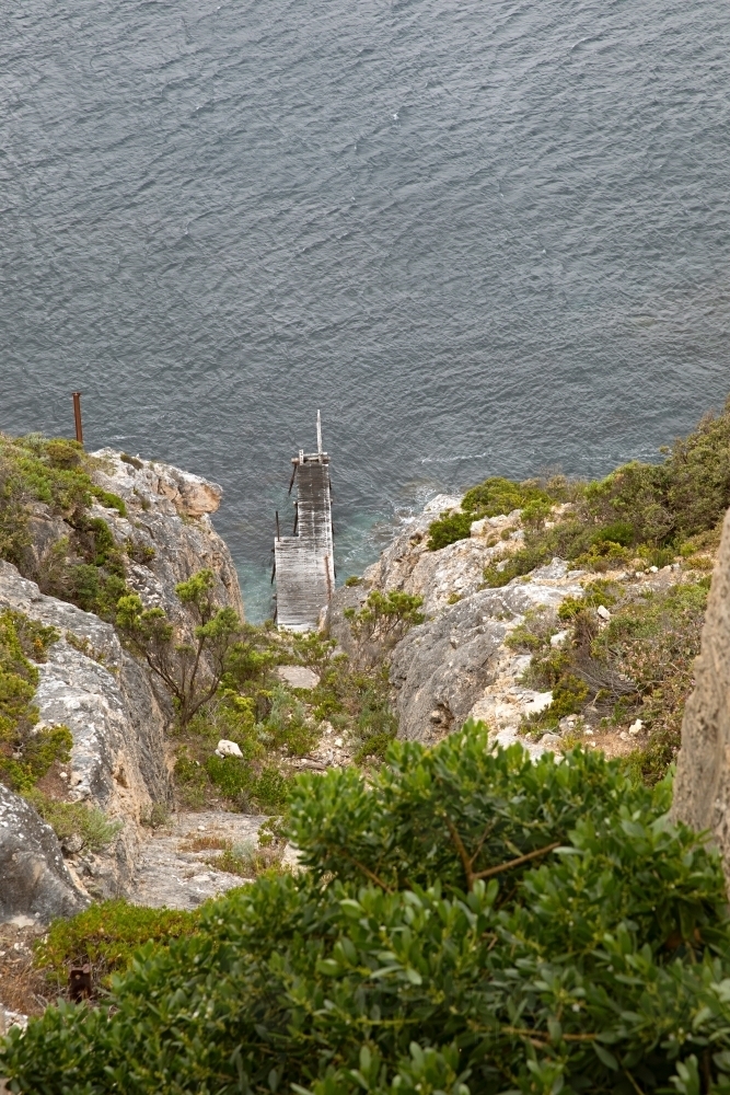 A coastal cliff overlooking a wooden dock on clear water - Australian Stock Image