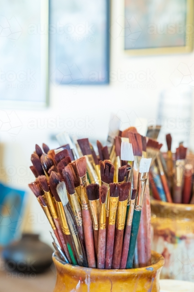 Image of Collection of artists paintbrushes in jar beside paint pots -  Austockphoto