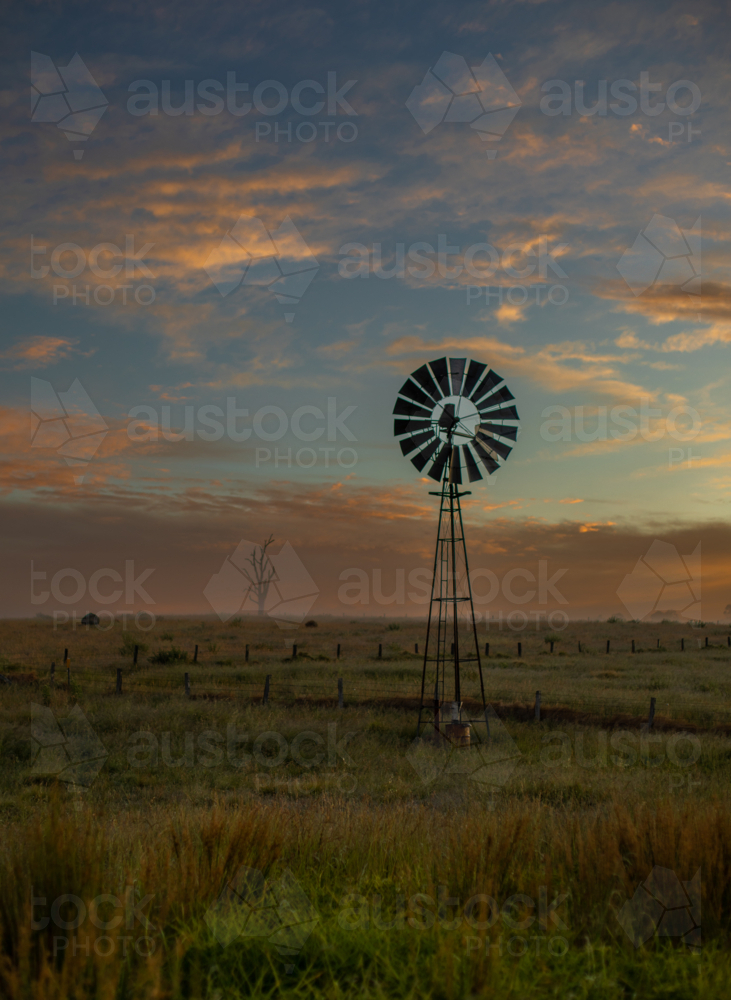 A colourful dawn sky and a windmill in a country field - Australian Stock Image