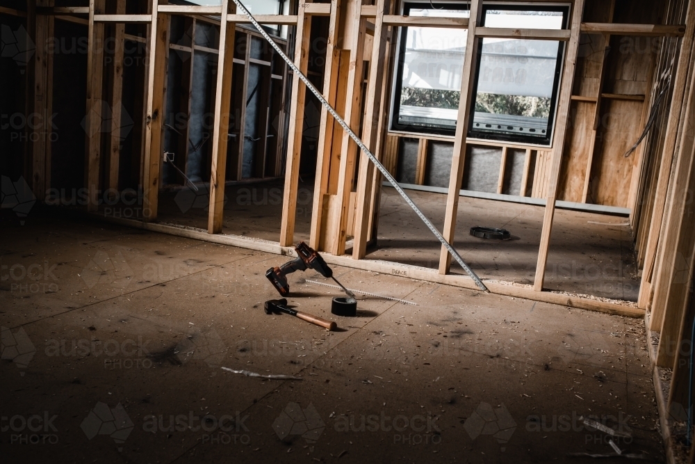 A construction site of a house being built with exposed wires and wooden beams, light shining in - Australian Stock Image