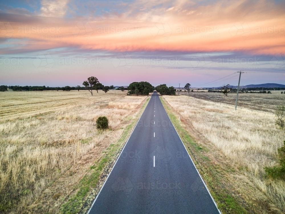 A country road leads of into the distance under a bank of coloured clouds - Australian Stock Image