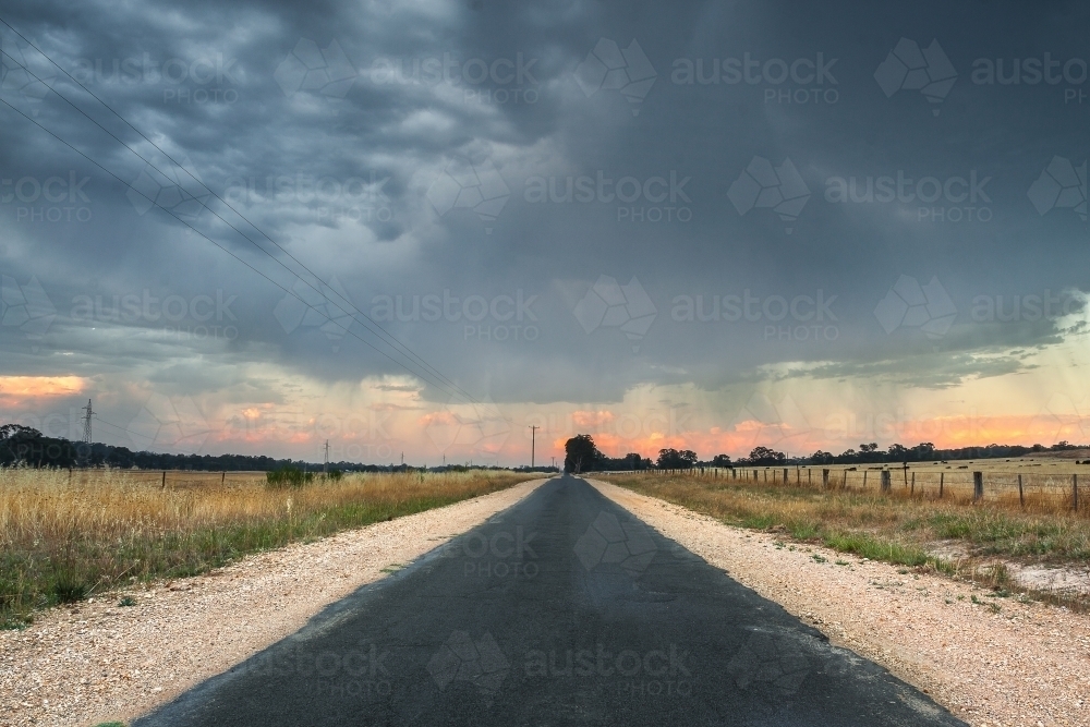 A country road leads off into the distance under storm clouds - Australian Stock Image