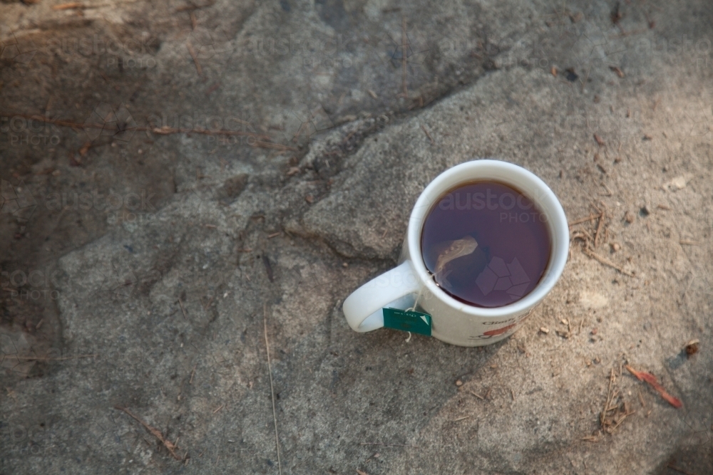 A cup of tea brewing on a rock outside - Australian Stock Image