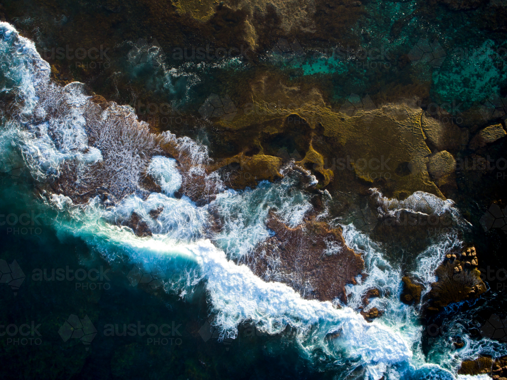 A dark ocean crashes over an exposed reef bed - Australian Stock Image