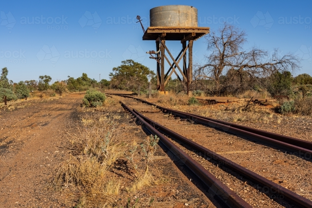 A derelict water tank on a high platform next to railway tracks running away into the distance - Australian Stock Image