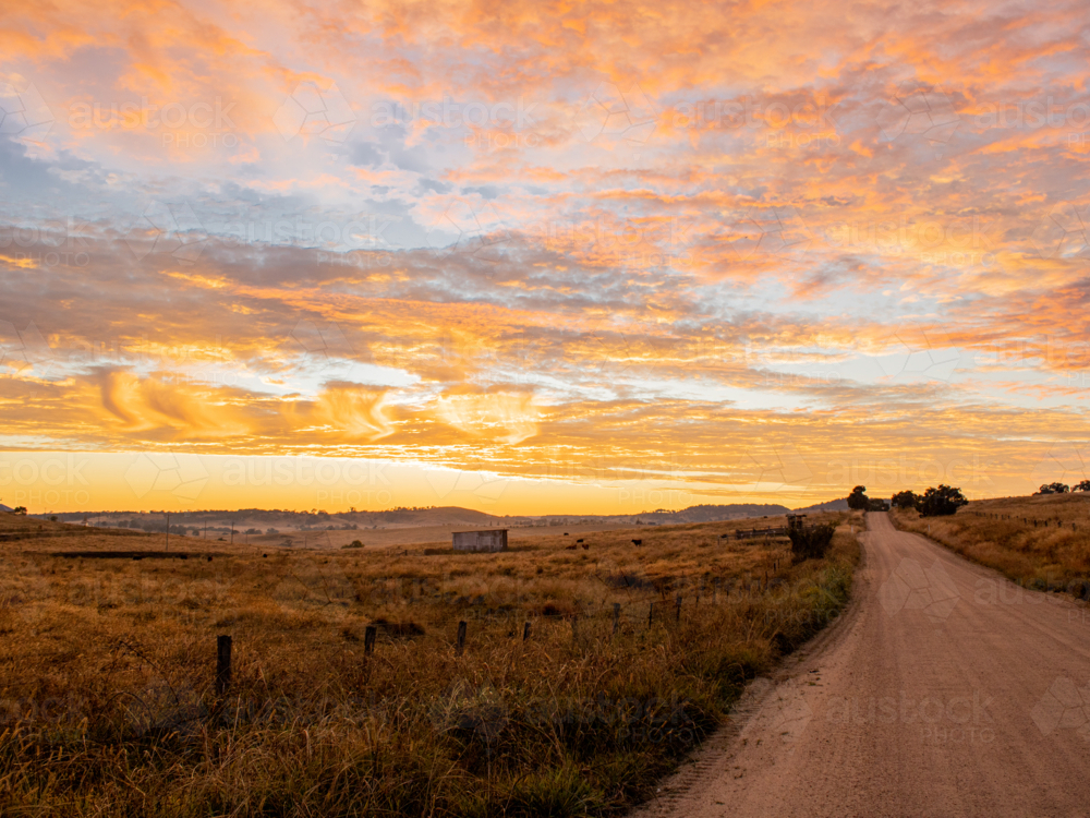 A dirt country road at dawn with orange clouds in sky - Australian Stock Image