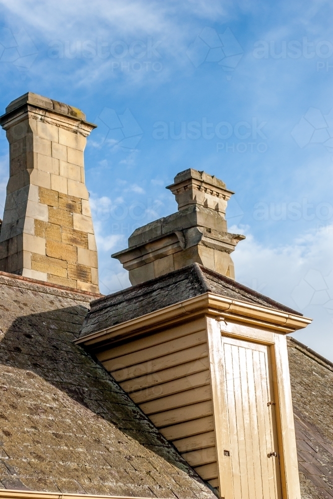 A dormer doorway in a slate roof with two elegant sandstone chimneys - Australian Stock Image