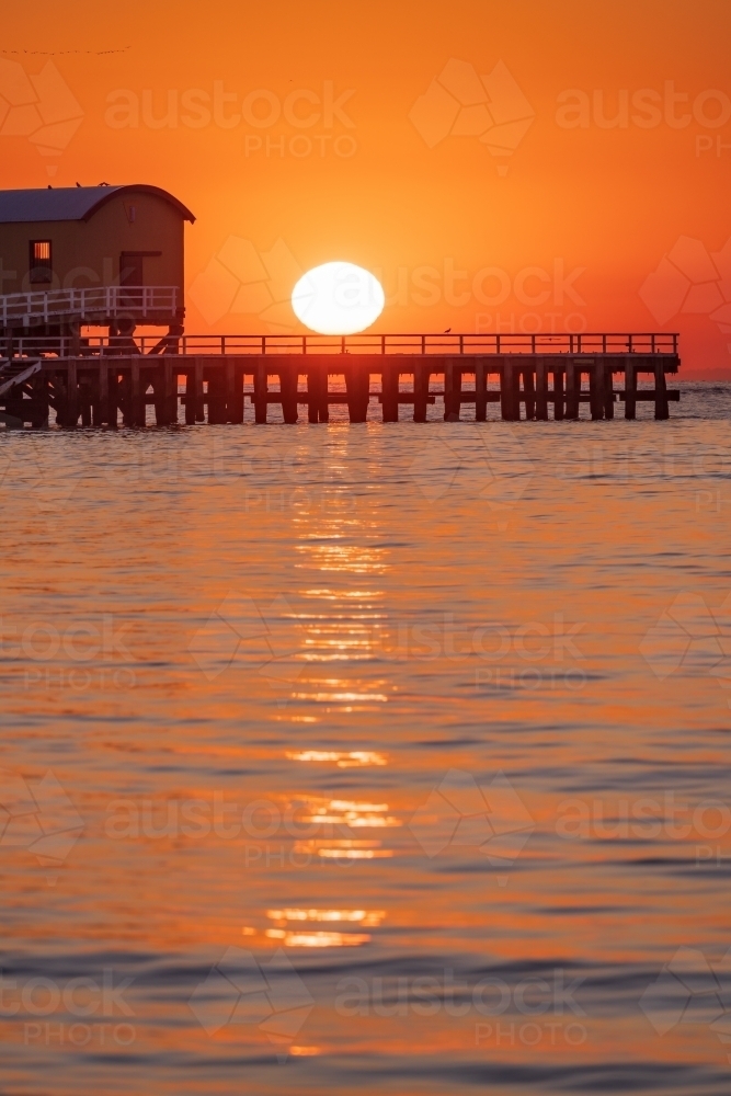 A dramatic golden sunrise over a coastal jetty and calm water - Australian Stock Image