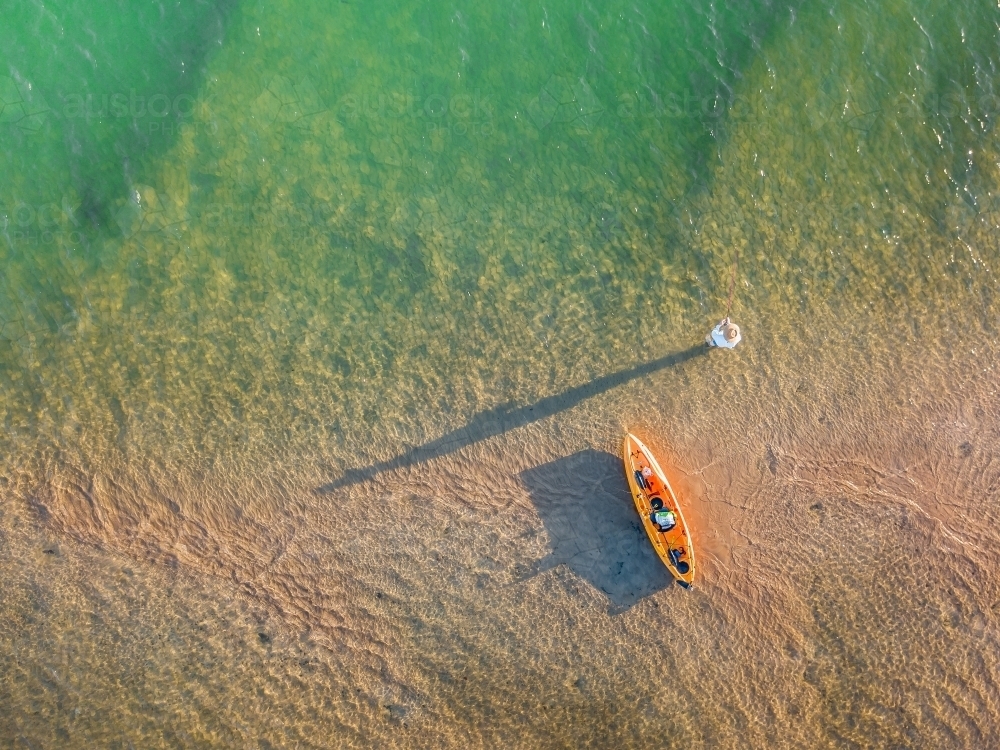 A fishermen alongside a kayak casting long shadows over a river - Australian Stock Image