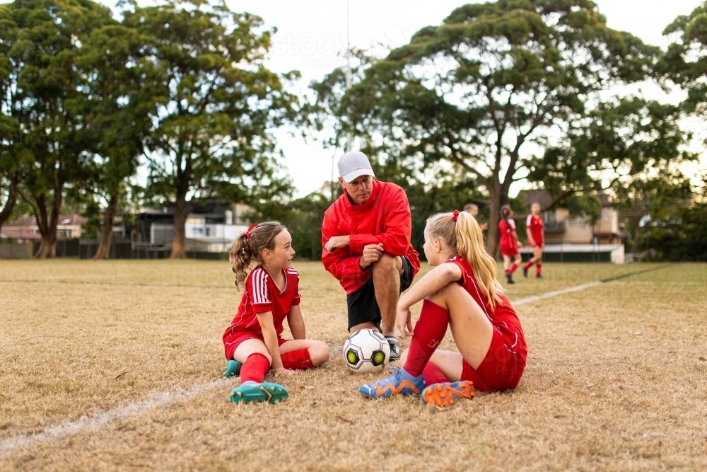 A football team coach kneeling down talking to girls in the football team - Australian Stock Image