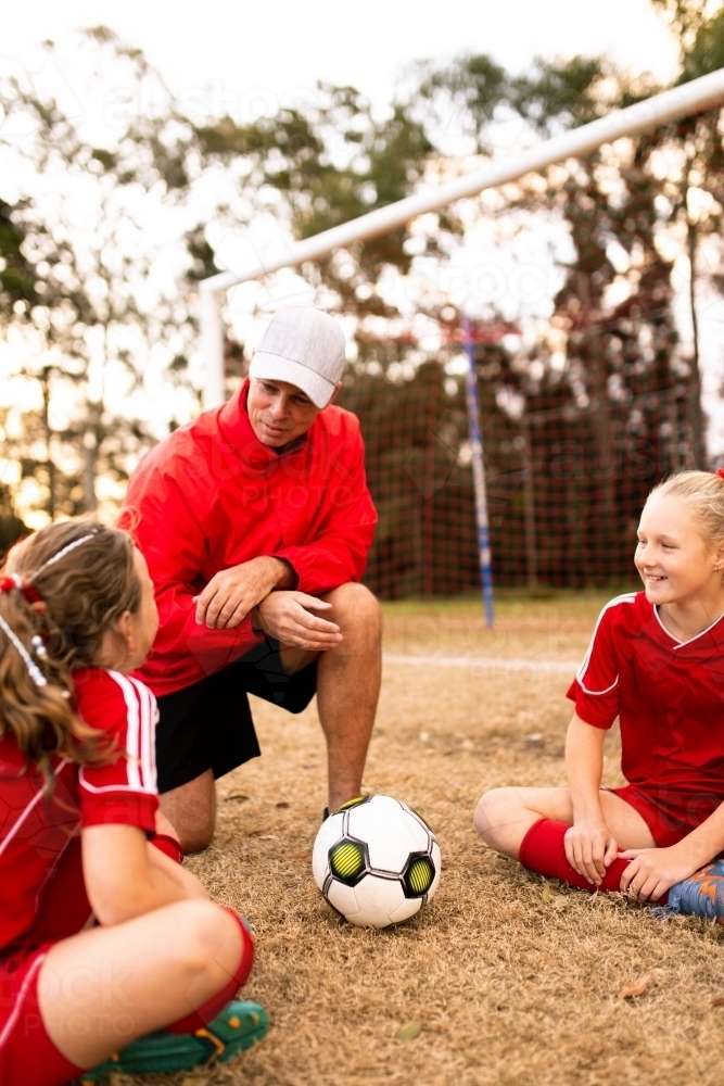 A football team coach kneeling down talking to girls in the football team - Australian Stock Image