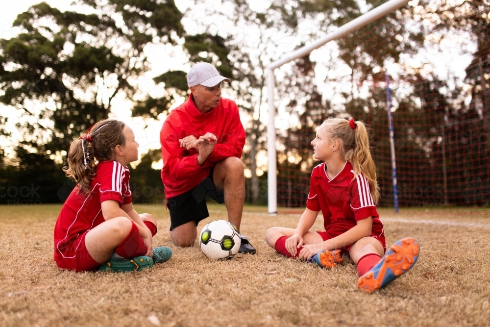 A football team coach kneeling down talking to girls in the football team - Australian Stock Image