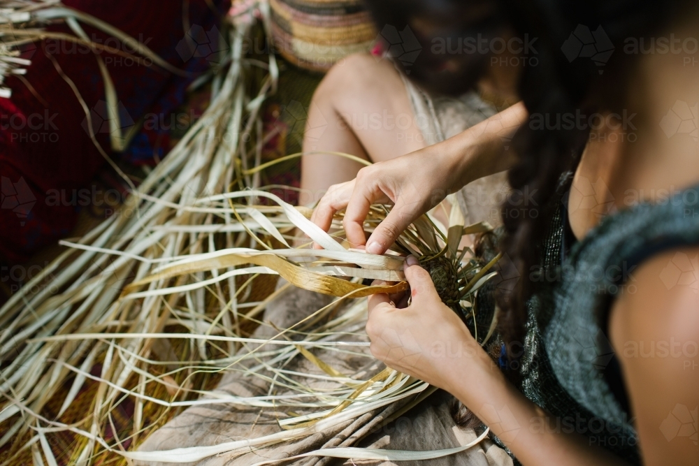 A girl with braided long hair working on a long fibrous material for weaving. - Australian Stock Image