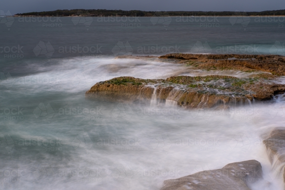 A grey dawn with waves breaking over rocks - Australian Stock Image