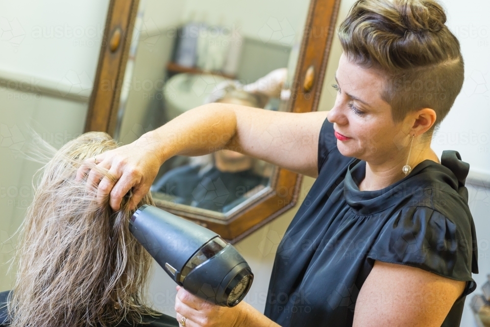 A hairdresser blow drying a ladies hair in a salon - Australian Stock Image