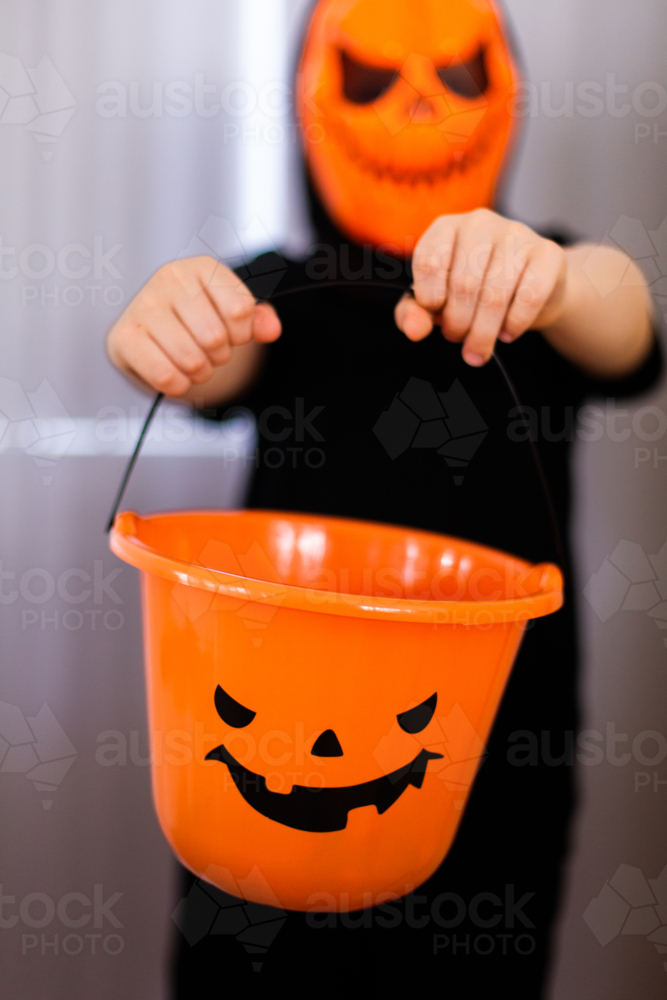 a halloween bucket being help up by a child in a costume - Australian Stock Image