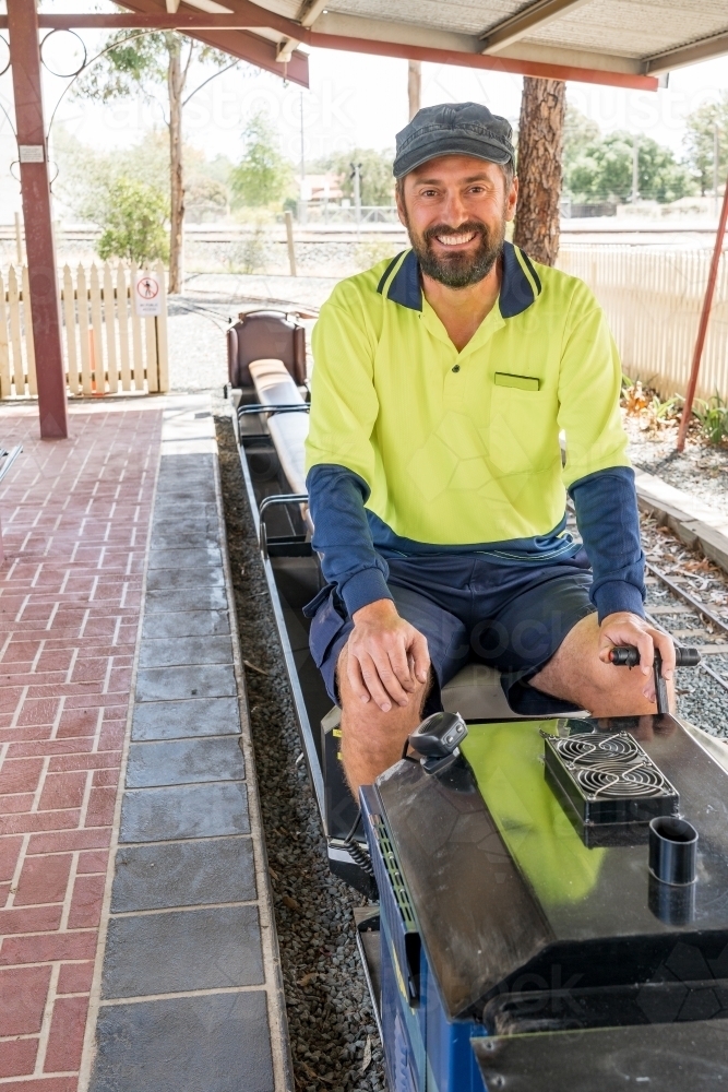 A happy train driver sitting aboard the controls of a miniature train - Australian Stock Image