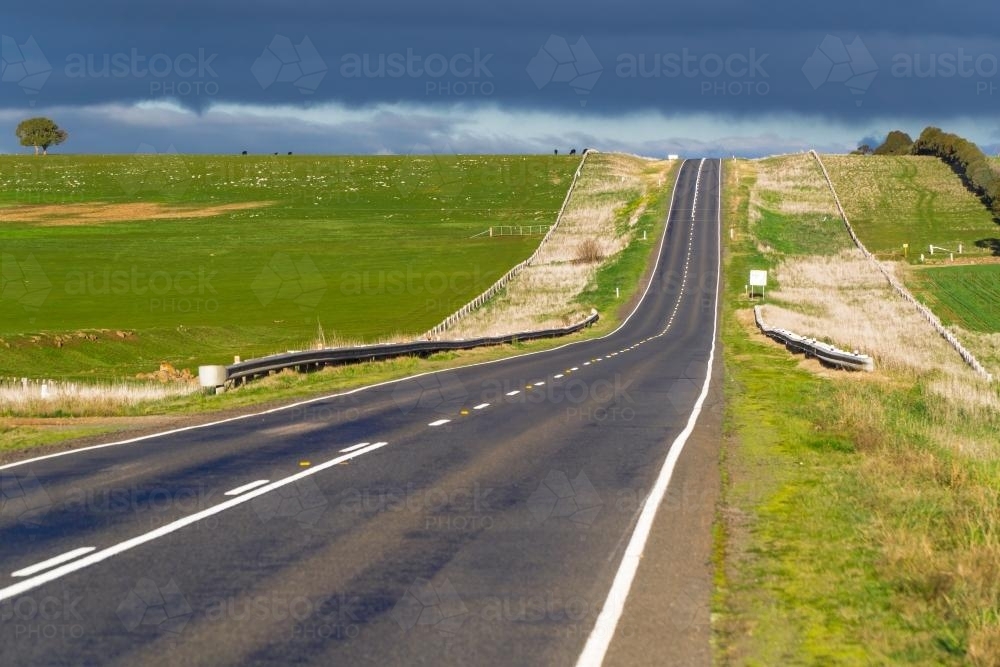 A highway leading up and over a green hill on a sunny day - Australian Stock Image