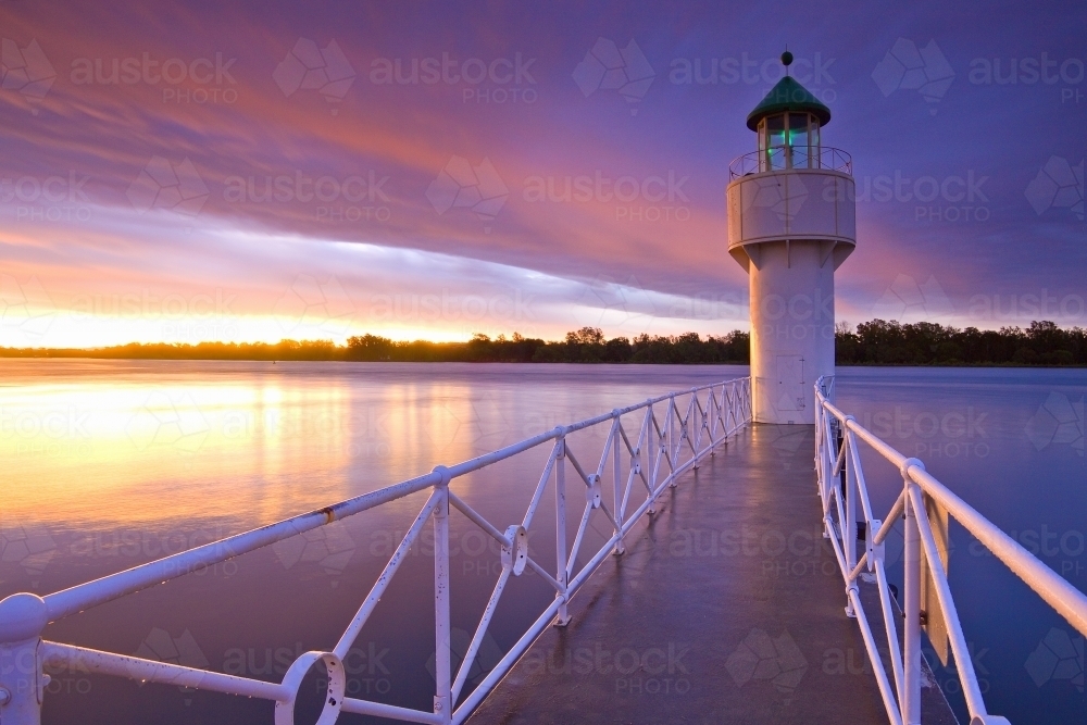 Image of A jetty leading out to a lighthouse under a colourful sunset ...