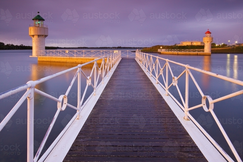 A jetty with white railings leading out to a pair of lighthouses at twilight - Australian Stock Image