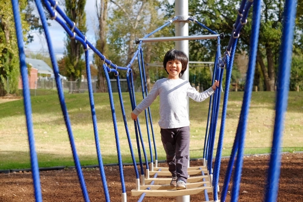 A kid crossing a wobbly bridge at the playground - Australian Stock Image