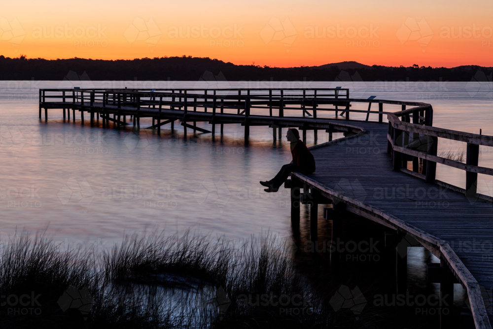 A lady in her 30's sitting on the edge of an observation deck over a lake. - Australian Stock Image