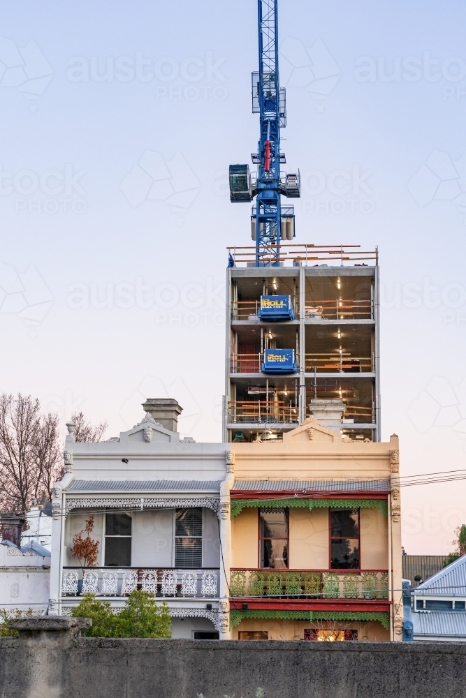 A large construction crane on a high rise building behind two storey terrace houses - Australian Stock Image