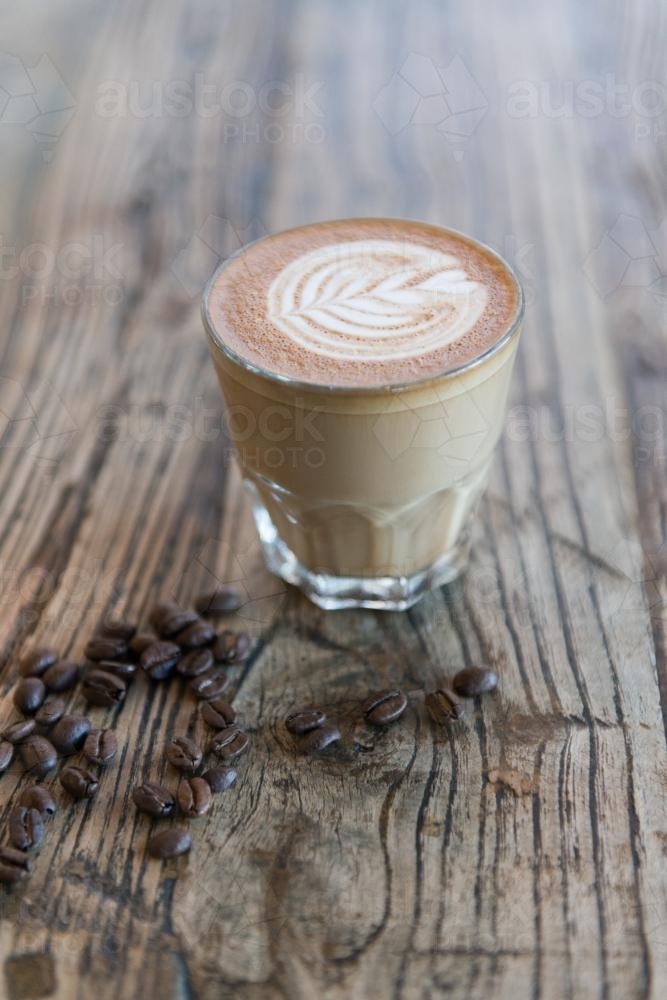 A latte on a wooden table with coffee beans - Australian Stock Image