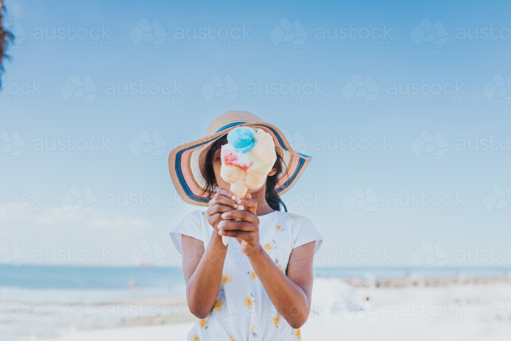 A little girl holding an ice cream at the beach with ocean as the background - Australian Stock Image