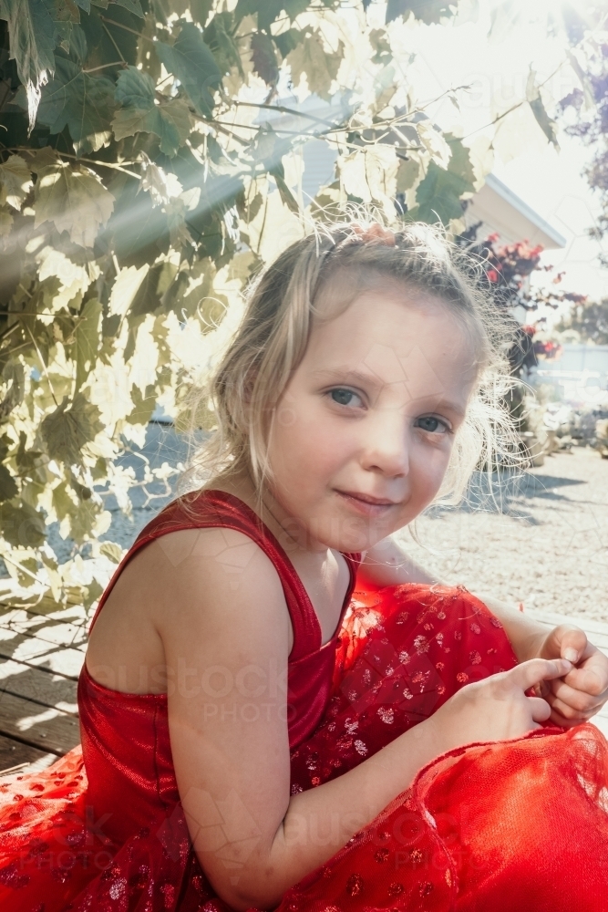 A little girl in a red dress in the garden. - Australian Stock Image