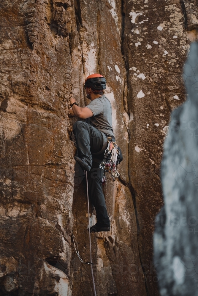 A male rock climber placing 'trad' gear into a cliff for a climbing route at Diamond Beach. - Australian Stock Image