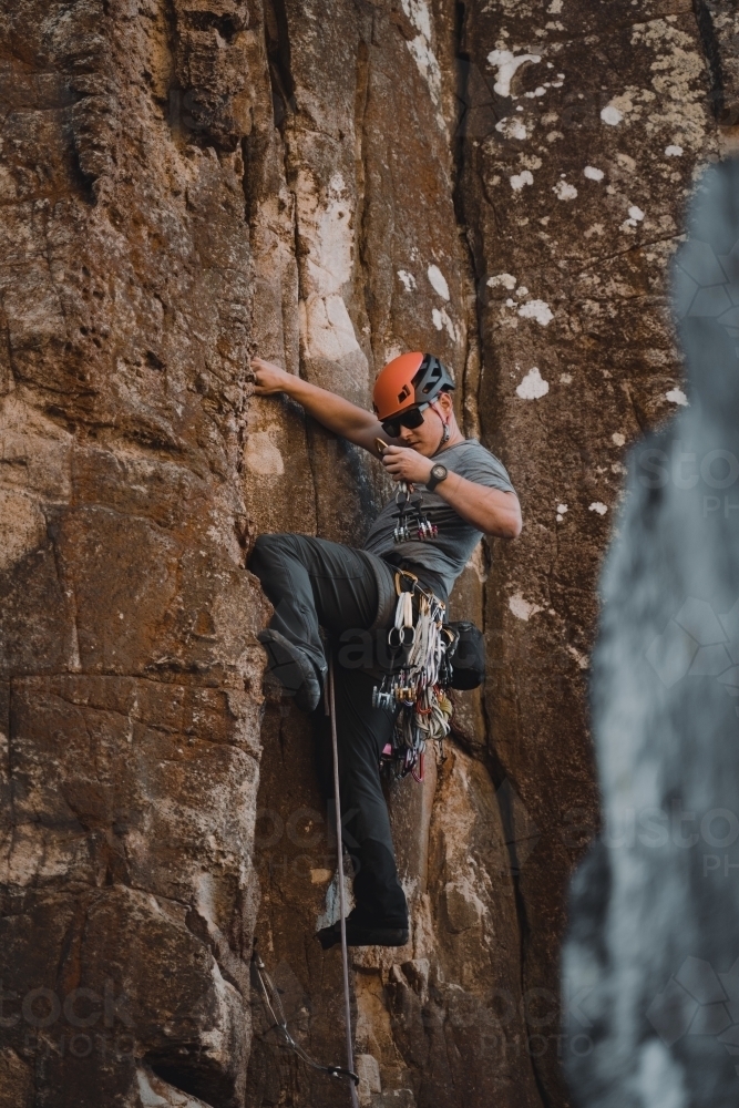 A male rock climber placing 'trad' gear into a cliff for a climbing route at Diamond Beach. - Australian Stock Image