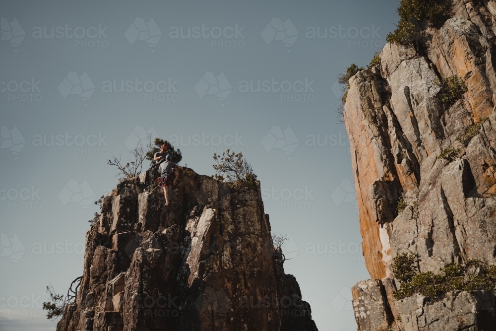 A male rock climber summits a climbing route at Diamond Beach. - Australian Stock Image