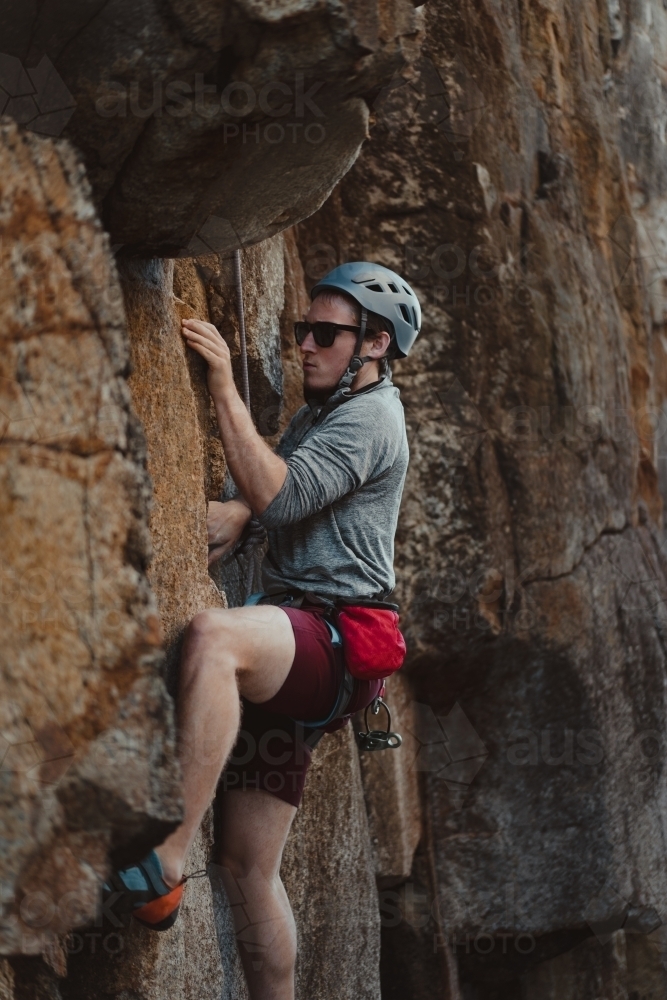 A male rock climber tackling a climbing route at Diamond Beach. - Australian Stock Image