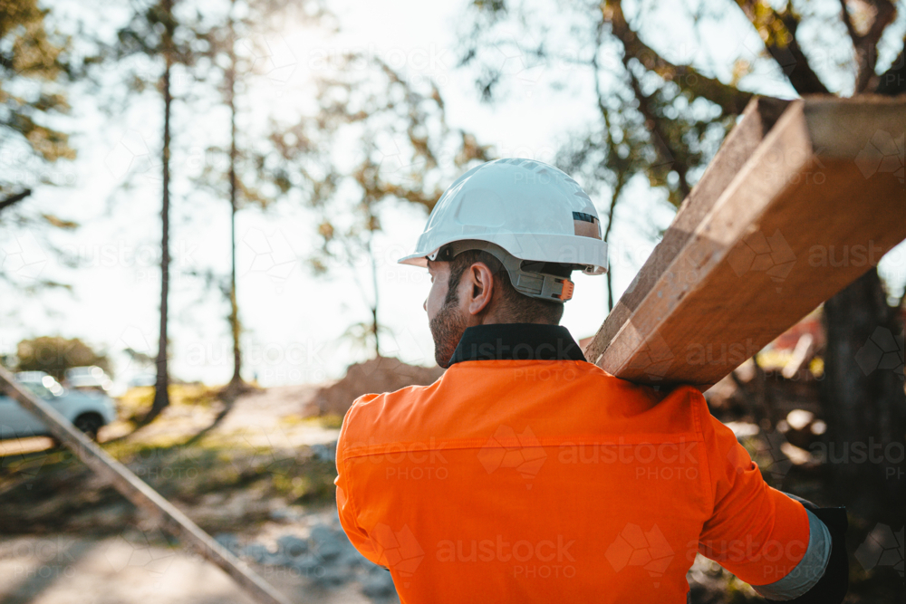 A man carrying a piece of lumber on his shoulder at a construction site - Australian Stock Image