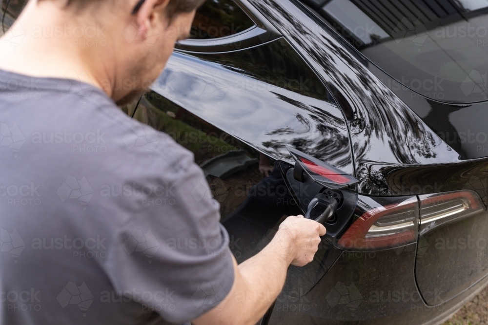 A man plugging in an electric Ev vehicle car to a home charger station plug - Australian Stock Image