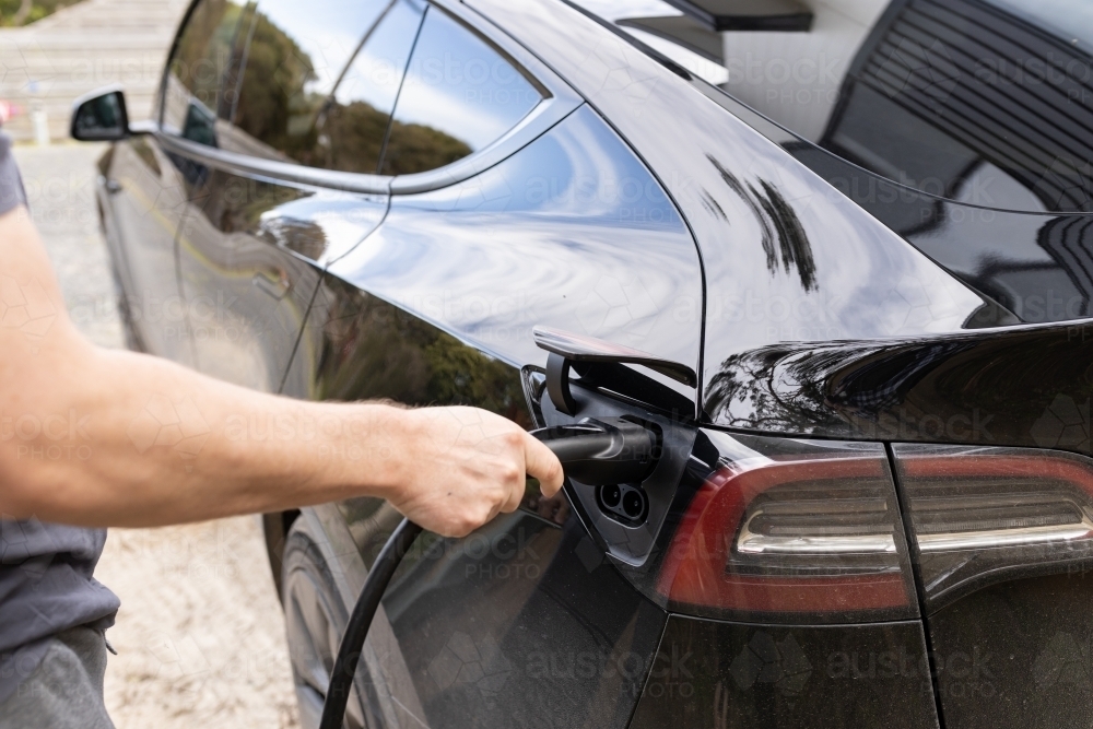 A man plugging in an electric Ev vehicle car to a home charger station plug - Australian Stock Image