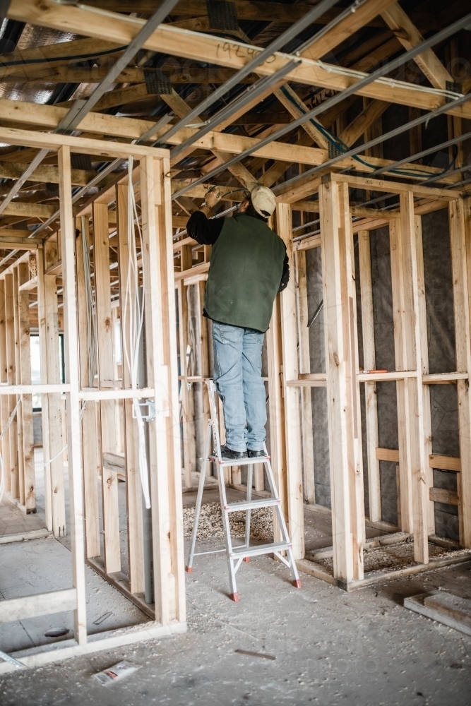 A man standing on a ladder doing some cabling work inside a newly built house - Australian Stock Image