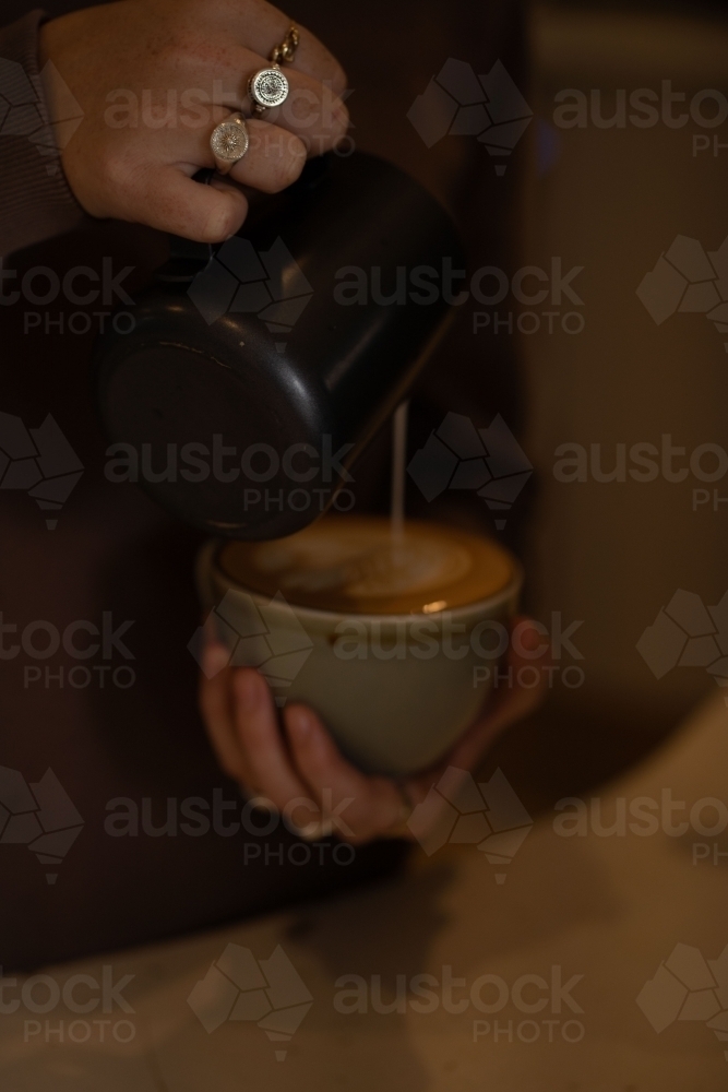 A milk poured from a black pitcher into a cup of coffee - Australian Stock Image