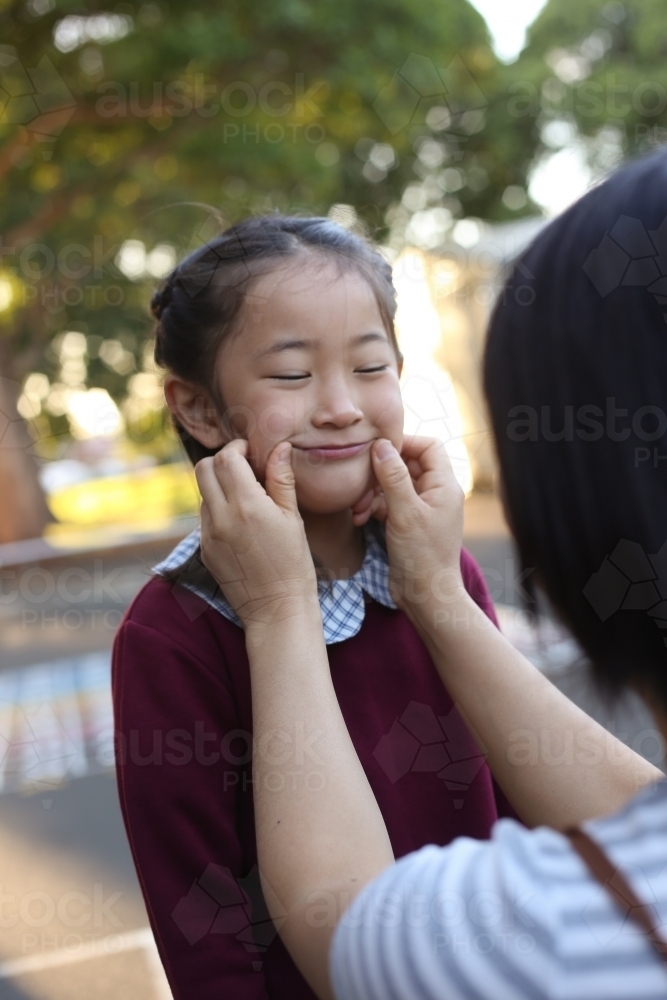 A mother pulling her daughter's cheeks in the school playground - Australian Stock Image