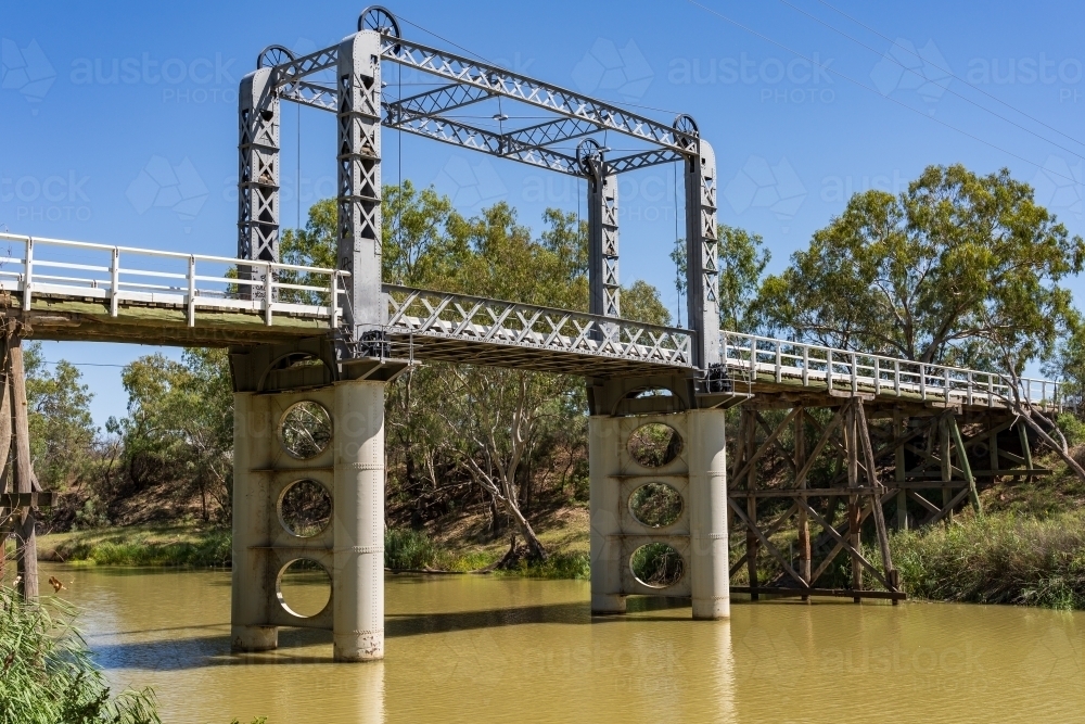 A murky river flowing under a disused lift span bridge - Australian Stock Image