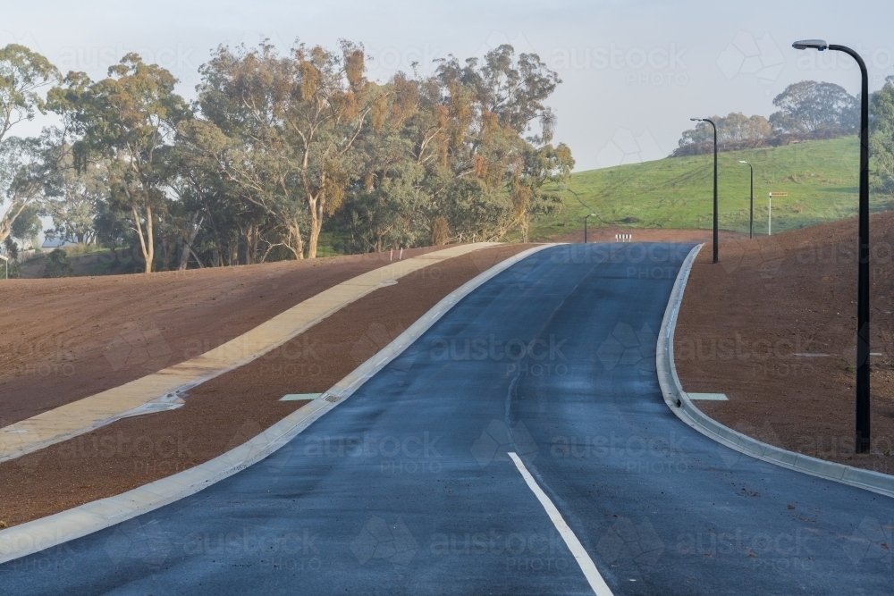 A newly laid bitumen road leading over a rise through a new residential development - Australian Stock Image