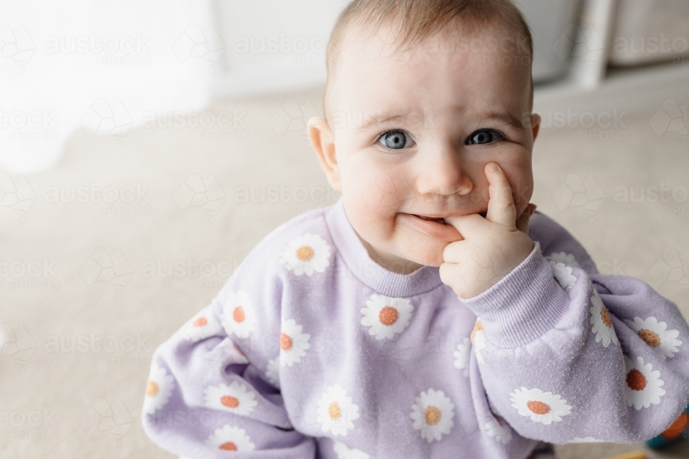 A one year old caucasian girl with blue eyes sitting on the ground inside - Australian Stock Image