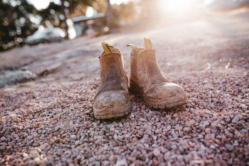 A pair of worn brown boots placed on a ground covered with small pebbles. - Australian Stock Image