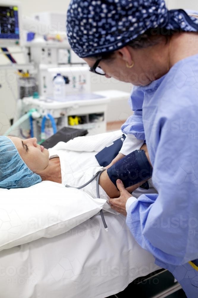 A patient lying on a bed in a hospital operating theatre with nurse taking blood pressure - Australian Stock Image