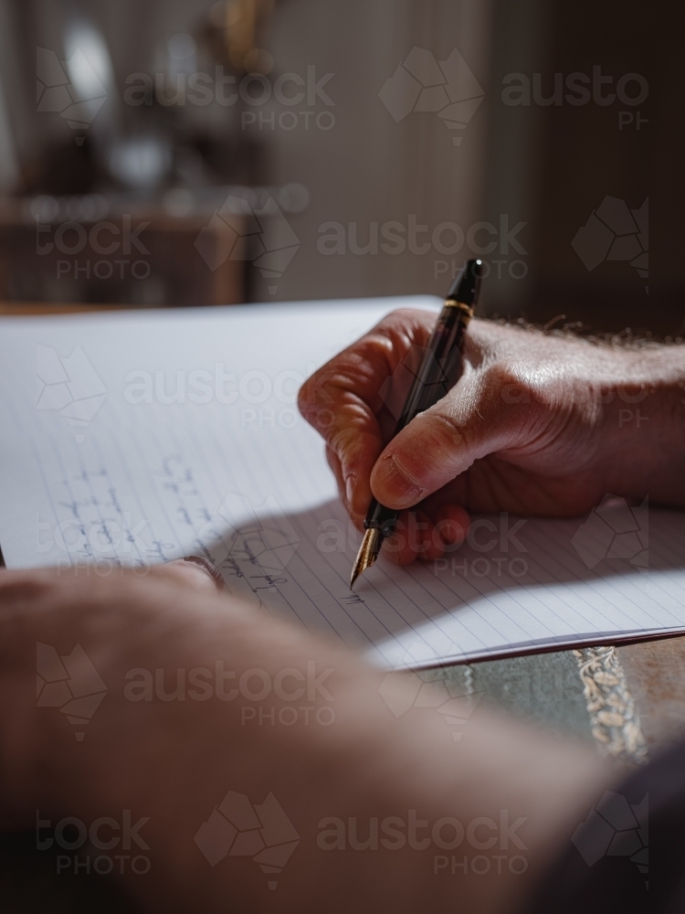 A person's hand holding a pen and writing on a lined notebook - Australian Stock Image